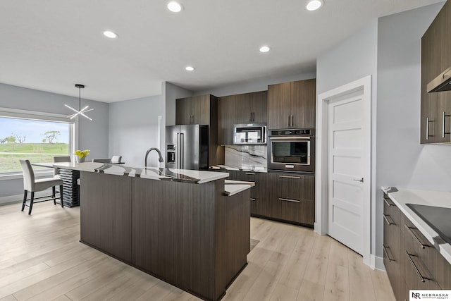 kitchen with light wood-type flooring, modern cabinets, a kitchen island with sink, and stainless steel appliances
