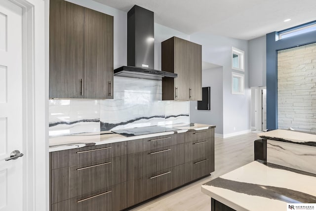 kitchen featuring decorative backsplash, light wood-style floors, light countertops, wall chimney exhaust hood, and black electric cooktop
