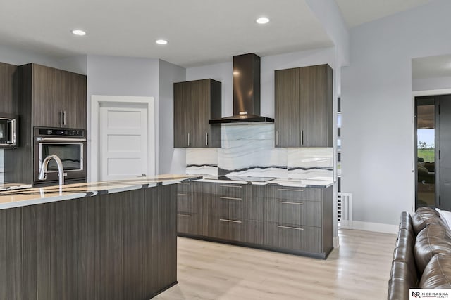 kitchen featuring wall chimney range hood, light countertops, modern cabinets, and wall oven