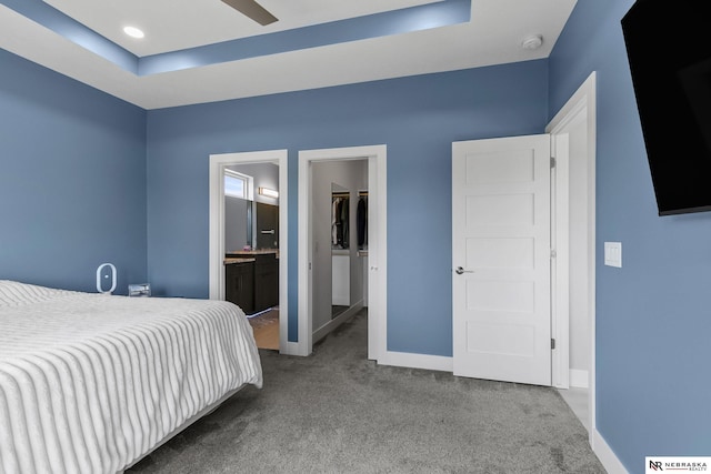 carpeted bedroom featuring baseboards, connected bathroom, a raised ceiling, and a walk in closet
