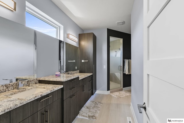 bathroom featuring a stall shower, wood finished floors, two vanities, a sink, and baseboards