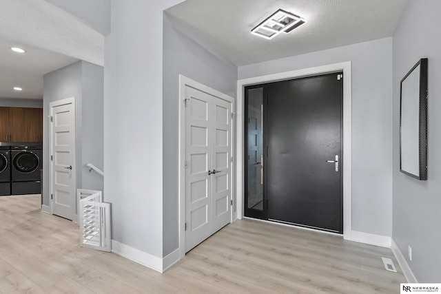 foyer entrance with baseboards, washing machine and dryer, light wood-style flooring, and visible vents