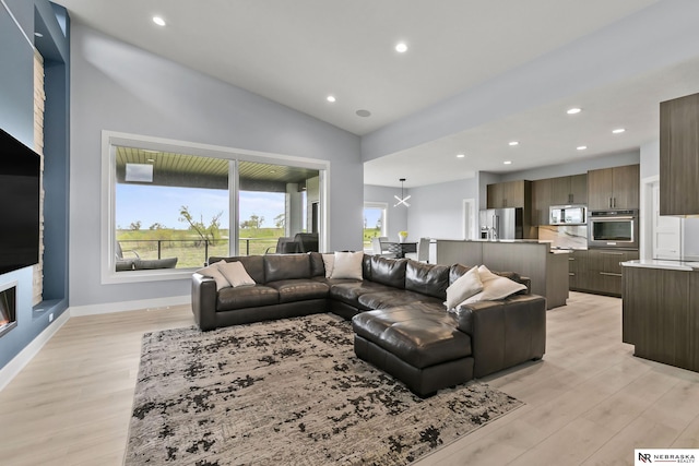 living area with baseboards, a glass covered fireplace, lofted ceiling, light wood-style floors, and recessed lighting