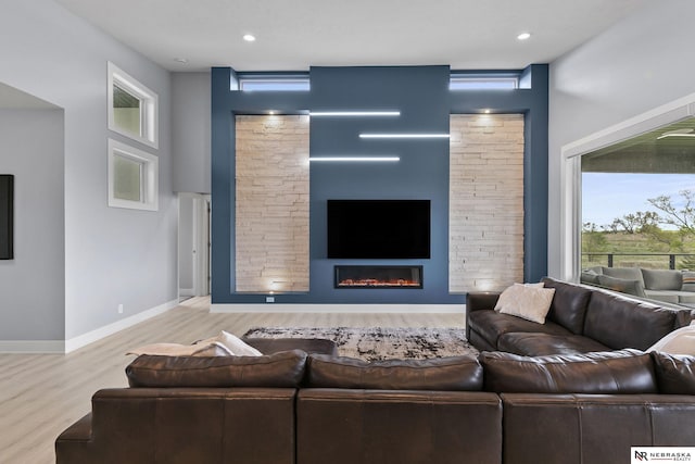 living area featuring a glass covered fireplace, baseboards, recessed lighting, and wood finished floors