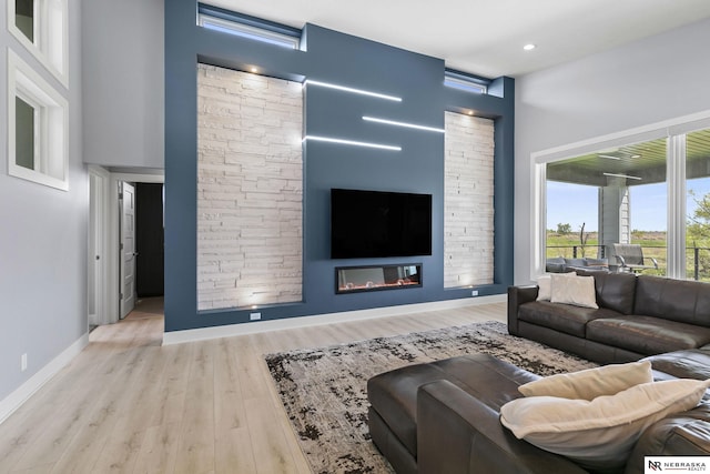 living area featuring baseboards, recessed lighting, a glass covered fireplace, and wood finished floors