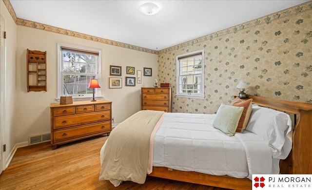 bedroom featuring visible vents, light wood-style floors, multiple windows, and wallpapered walls