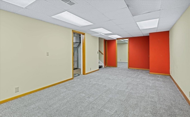finished below grade area featuring visible vents, baseboards, stairway, light colored carpet, and a paneled ceiling