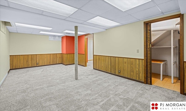 finished basement with carpet flooring, wood walls, wainscoting, and a paneled ceiling