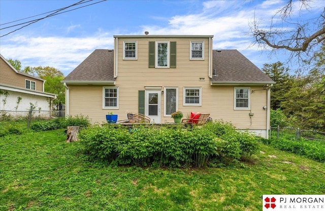 back of property featuring a lawn, a shingled roof, and fence