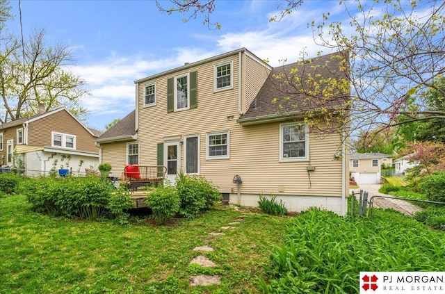 back of property with a lawn, roof with shingles, a wooden deck, and fence