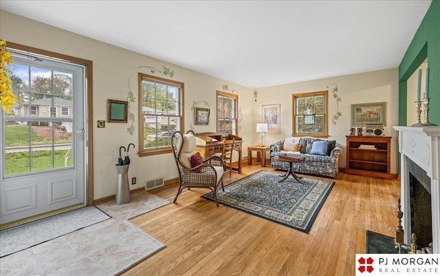 living area featuring visible vents, a fireplace with flush hearth, light wood finished floors, and a wealth of natural light