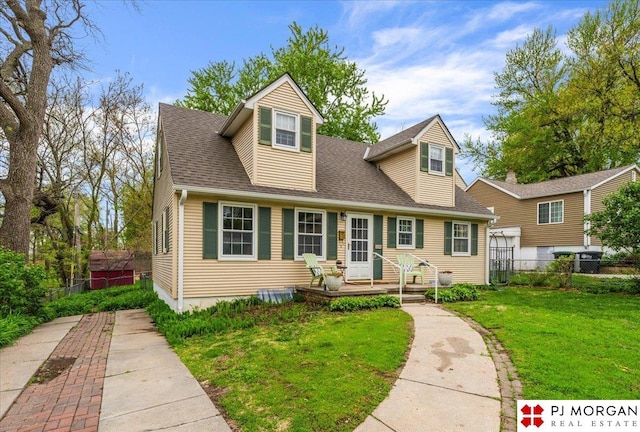 cape cod home with roof with shingles, fence, and a front yard