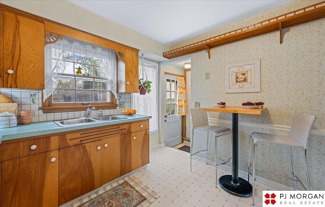kitchen featuring baseboards, light countertops, brown cabinets, tasteful backsplash, and a sink
