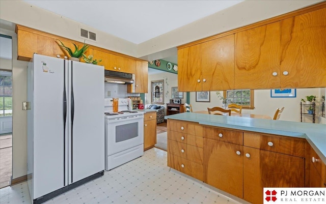 kitchen featuring brown cabinetry, under cabinet range hood, white appliances, and visible vents