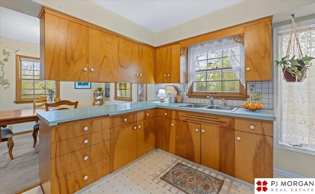kitchen with a sink, decorative backsplash, brown cabinetry, and a peninsula