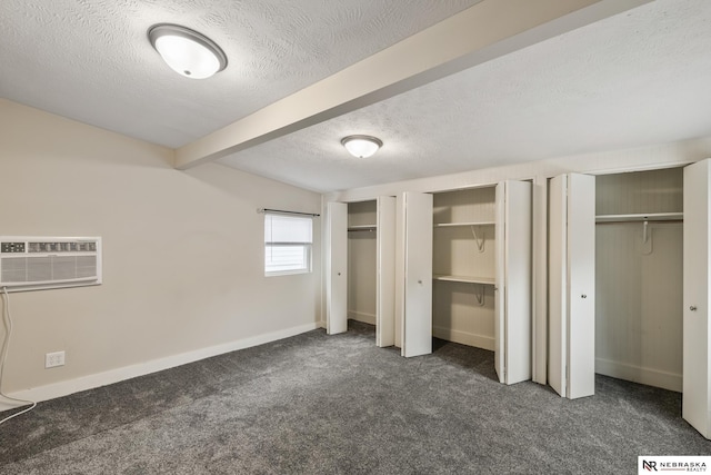unfurnished bedroom with a textured ceiling, a wall mounted AC, baseboards, carpet flooring, and multiple closets