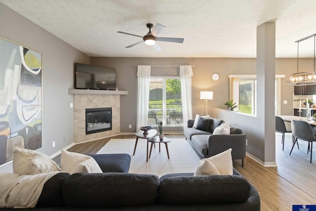 living area featuring light wood-type flooring, a chandelier, a fireplace, a ceiling fan, and baseboards