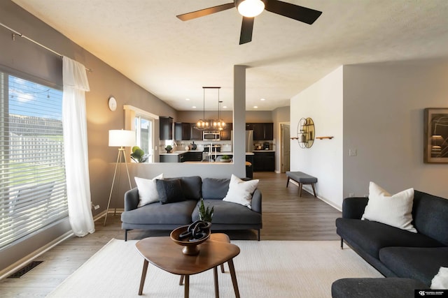 living area with light wood-style flooring, ceiling fan, baseboards, and a chandelier
