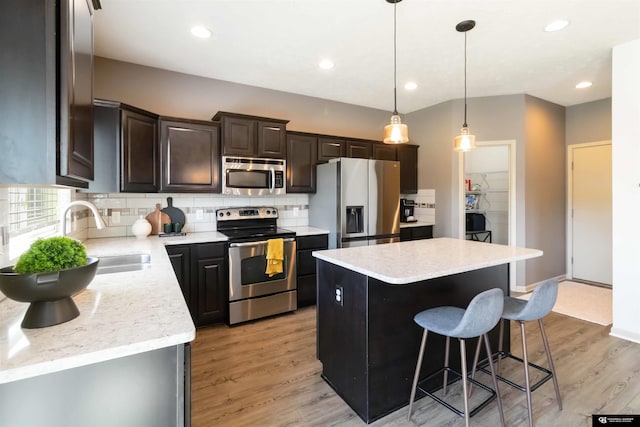 kitchen featuring stainless steel appliances, a sink, a center island, tasteful backsplash, and a kitchen bar
