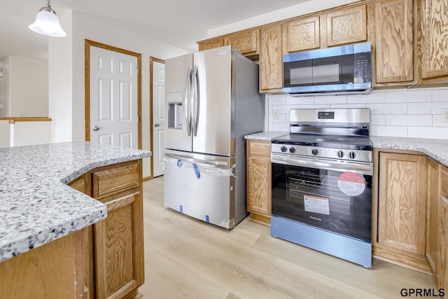 kitchen with brown cabinets, appliances with stainless steel finishes, light wood finished floors, tasteful backsplash, and pendant lighting