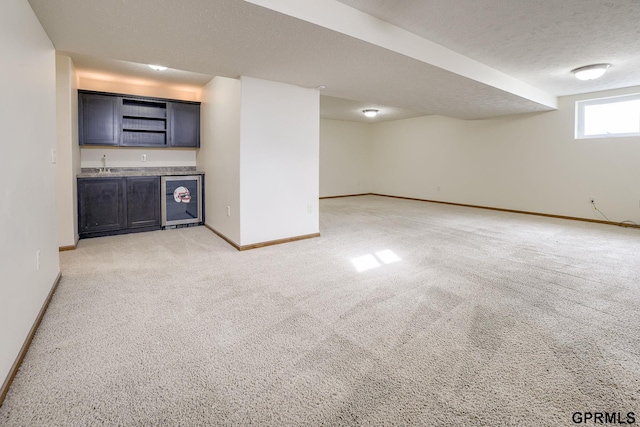 below grade area featuring light carpet, a sink, beverage cooler, indoor wet bar, and baseboards