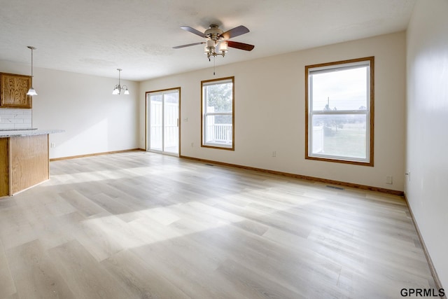 unfurnished living room featuring baseboards, visible vents, ceiling fan with notable chandelier, and light wood-type flooring