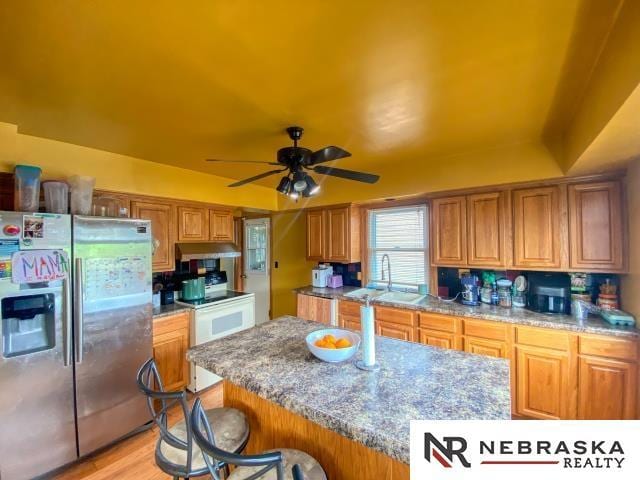 kitchen with white range with electric stovetop, stainless steel fridge, a sink, a kitchen breakfast bar, and under cabinet range hood