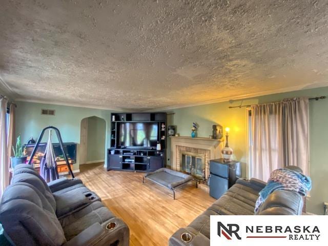 living room with a fireplace, arched walkways, a textured ceiling, wood finished floors, and visible vents