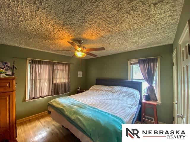 bedroom featuring baseboards, a ceiling fan, a textured ceiling, and wood finished floors