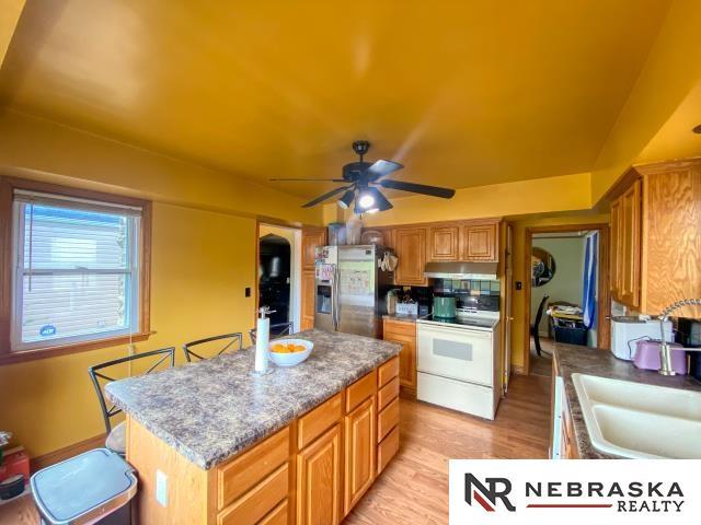 kitchen with electric range, ceiling fan, stainless steel fridge, a sink, and under cabinet range hood