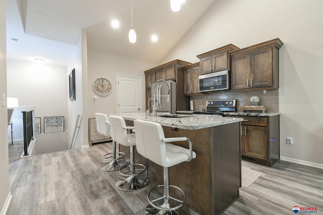 kitchen with a breakfast bar area, a kitchen island with sink, backsplash, appliances with stainless steel finishes, and light wood finished floors