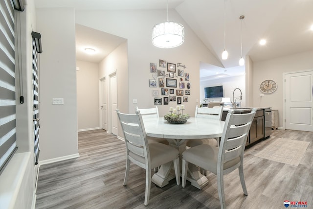 dining space with baseboards, light wood finished floors, high vaulted ceiling, and an inviting chandelier