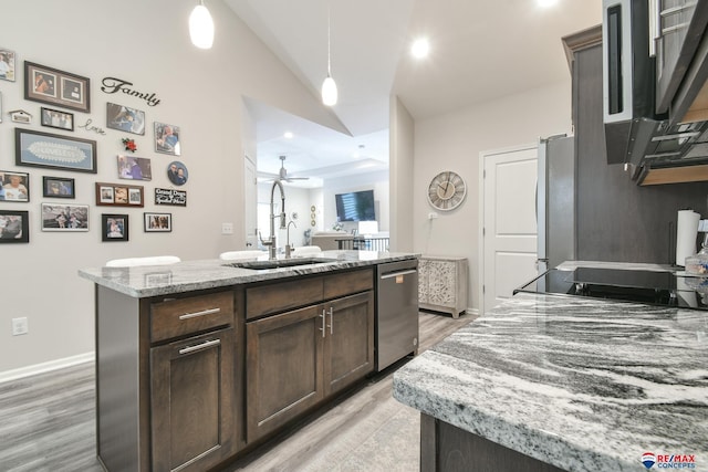 kitchen featuring a kitchen island with sink, dark brown cabinetry, a sink, light wood-style floors, and stainless steel appliances