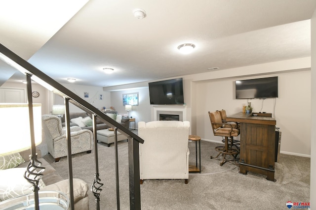 living room featuring a glass covered fireplace, baseboards, carpet flooring, and stairs