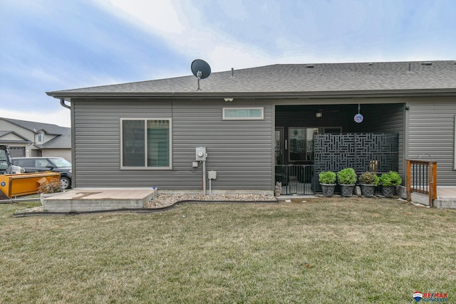 rear view of property featuring a lawn and a shingled roof