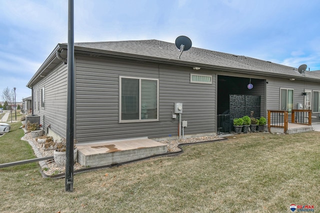 rear view of house featuring central AC unit, roof with shingles, and a yard