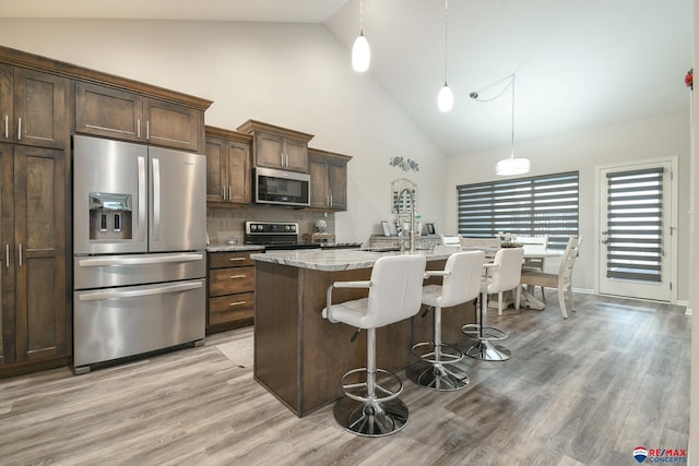 kitchen with light wood-style floors, high vaulted ceiling, an island with sink, stainless steel appliances, and a kitchen bar