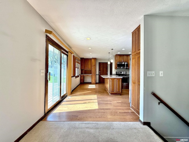 kitchen featuring brown cabinets, light countertops, range, stainless steel microwave, and baseboards