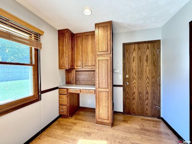 kitchen featuring brown cabinets, built in study area, light wood-style floors, light countertops, and a textured ceiling