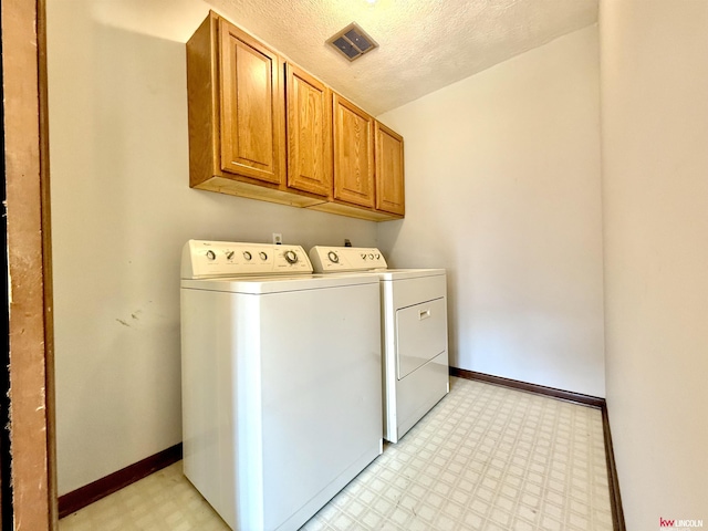clothes washing area with washer and dryer, cabinet space, light floors, a textured ceiling, and baseboards