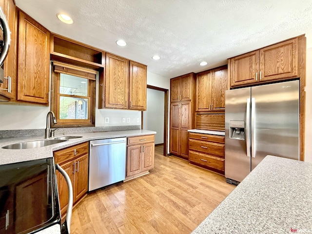 kitchen with a sink, brown cabinetry, a textured ceiling, light wood-type flooring, and appliances with stainless steel finishes