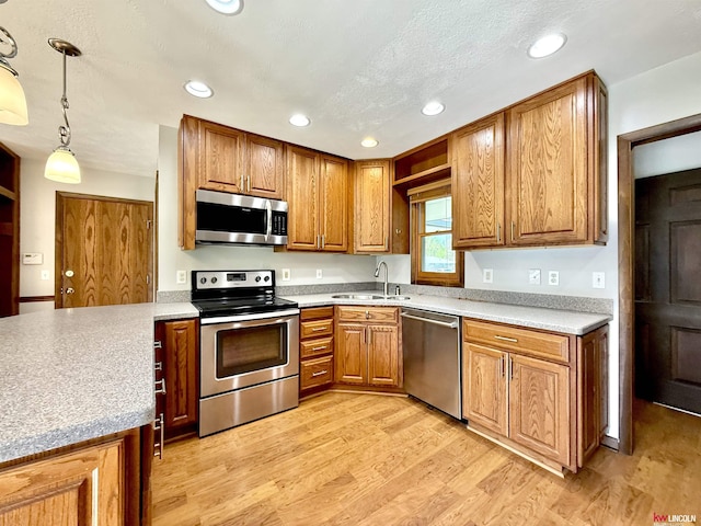 kitchen featuring stainless steel appliances, brown cabinets, light wood-style flooring, and a sink