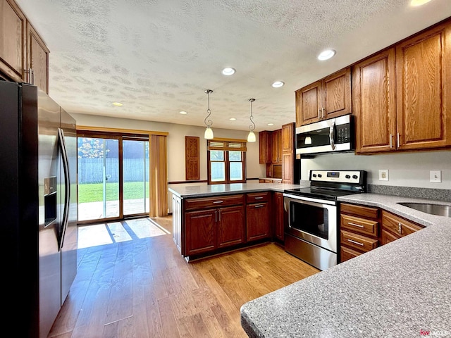 kitchen with recessed lighting, a textured ceiling, light wood finished floors, a peninsula, and stainless steel appliances