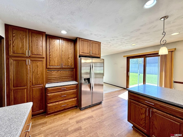 kitchen with brown cabinets, stainless steel fridge, light wood-style floors, a textured ceiling, and pendant lighting
