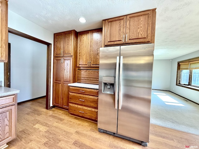 kitchen featuring a textured ceiling, stainless steel fridge, brown cabinetry, and light wood-type flooring