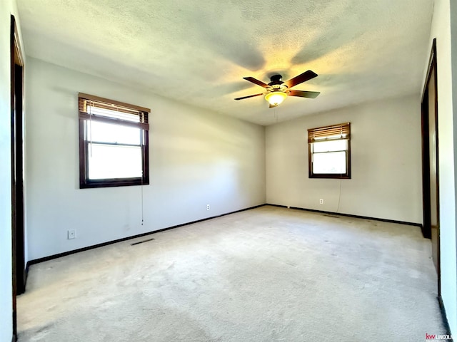 empty room featuring a textured ceiling, baseboards, visible vents, ceiling fan, and light carpet