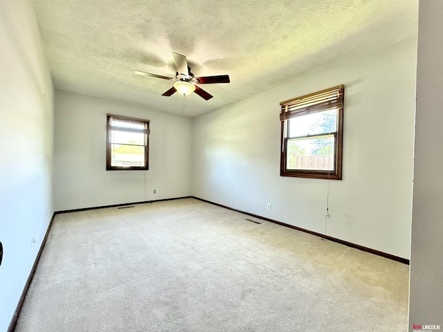 empty room with a ceiling fan, light carpet, a textured ceiling, and baseboards