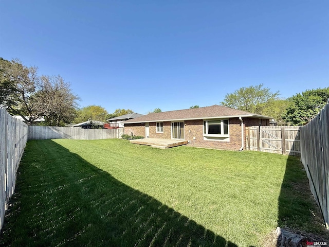 rear view of property with a fenced backyard, a wooden deck, brick siding, and a lawn