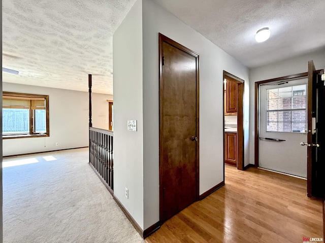 corridor with baseboards, a textured ceiling, and light wood-style floors