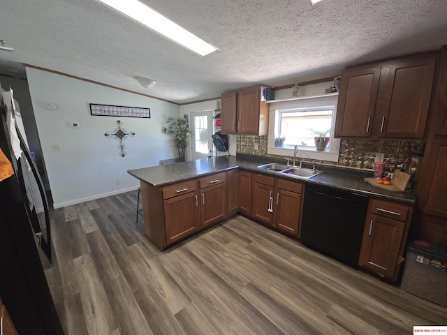 kitchen with a sink, dark countertops, a peninsula, and dishwasher
